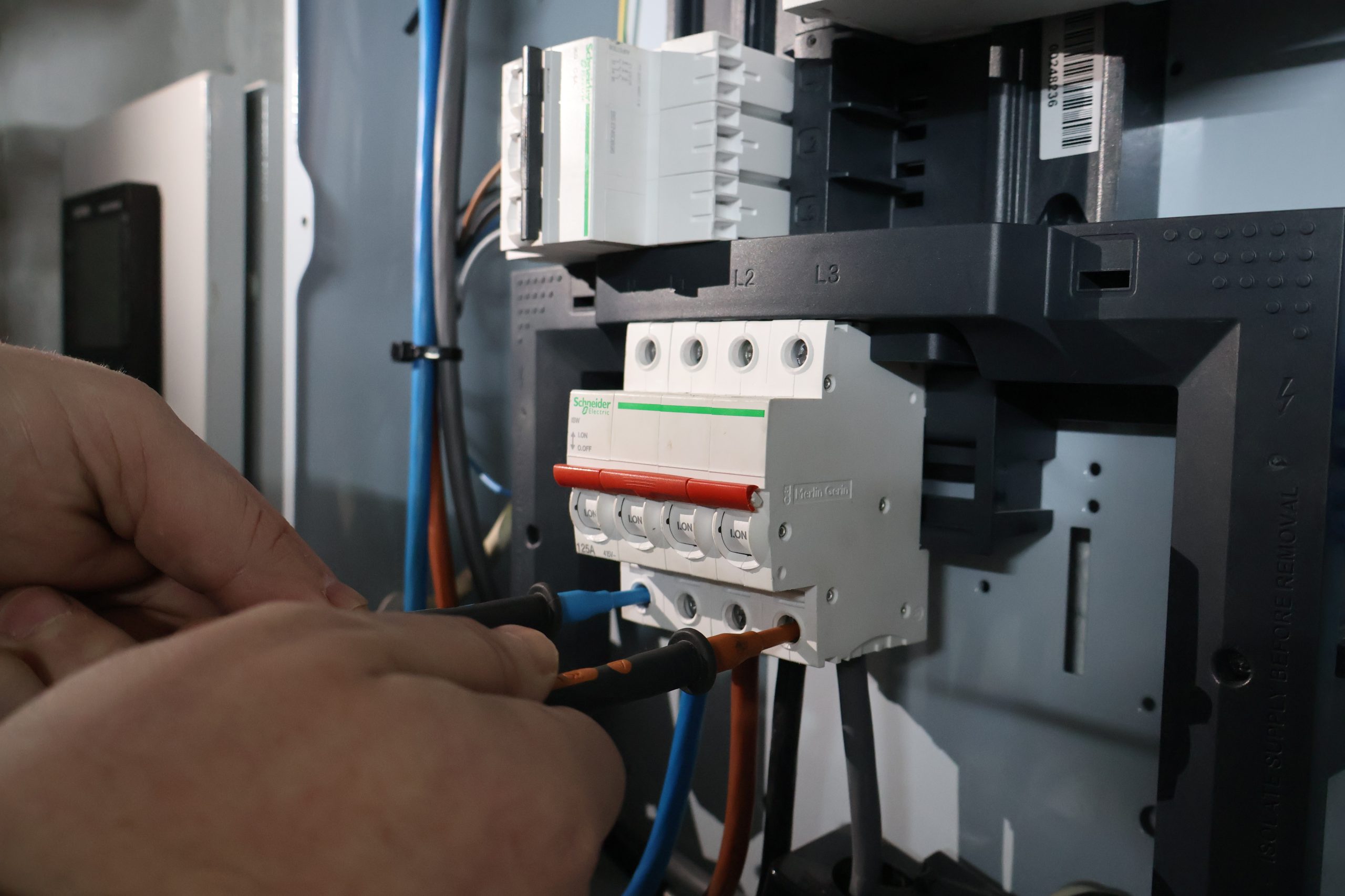 Close-up of a hand holding a multimeter probe, testing an electrical component